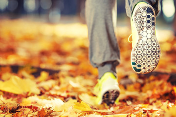 Runner woman feet running on autumn road closeup on shoe. Female fitness model outdoors fall jog workout on a road covered with fallen leaves. Sports healthy lifestyle concept.