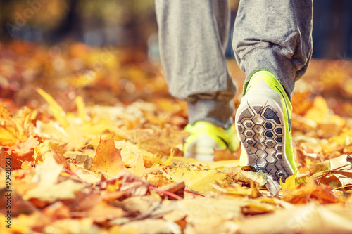 Runner woman feet running on autumn road closeup on shoe. Female fitness model outdoors fall jog workout on a road covered with fallen leaves. Sports healthy lifestyle concept.