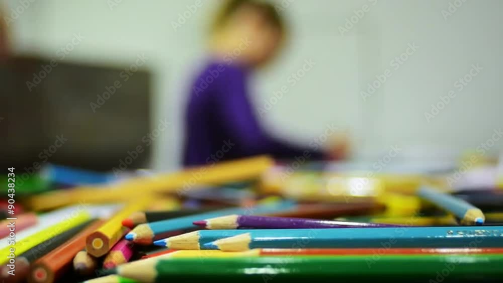 Slow motion of a color pencils in the foreground and a blurry girl shape drawing and painting in the background Slow motion of a color pencils in the foreground and a blurry girl shape drawing and painting in the background