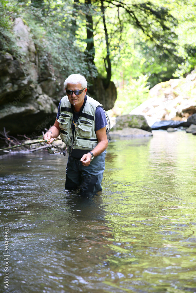 Fly-fisherman fishing in river on summer season Fly-fisherman fishing in river on summer season