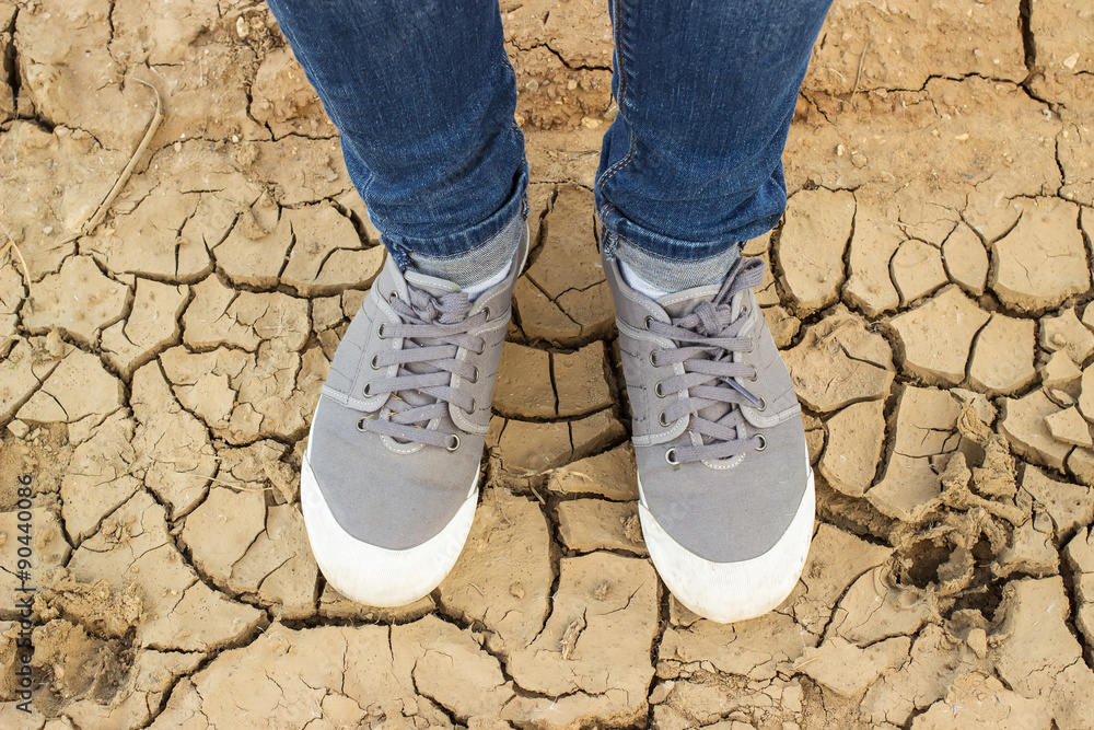 feet in sneakers and blue jeans standing on the cracked soil