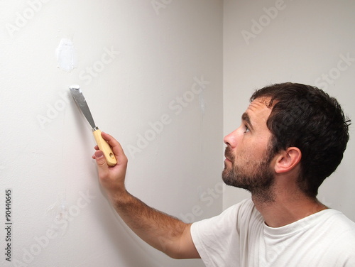 Black-haired man covering a hole in the white wall with a bricklayer cement (putty).
