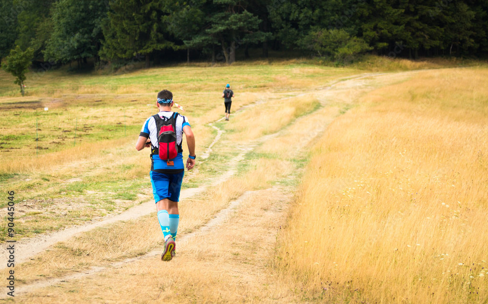 male ultra runner with backpack training on a meadow in summer male ultra runner with backpack training on a meadow in summer