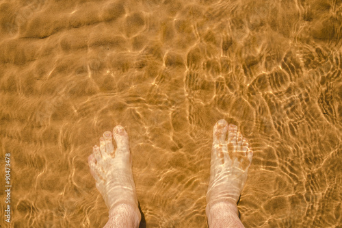 view from above on their own male legs, standing in the water on the sand