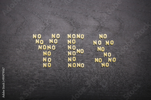 фотографія The answer  yes made up of a set of words no, with small pasta letters on a dark background of a wooden board, showing the hidden meaning and ambiguity of the agreement