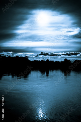 Moonlight in the clouds over a lake