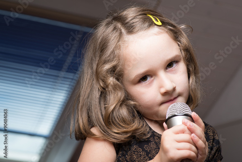 Little cute girl singing karaoke on microphone at home