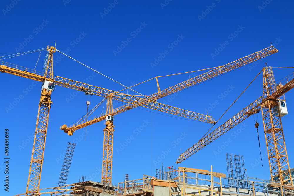 Three construction cranes and building against blue sky.