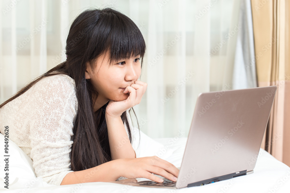 Asian Woman lying on a bed at home and she works on a laptop Asian Woman lying on a bed at home and she works on a laptop