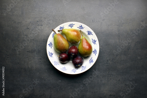 Fresh pears and plums on ornamental plate and grey kitchen table