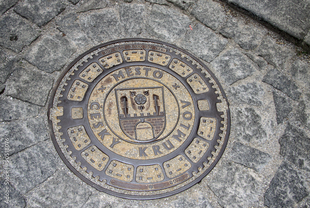 Round steel sewer manhole on old cobblestone road in Cesky Krumlov, Czech Republic