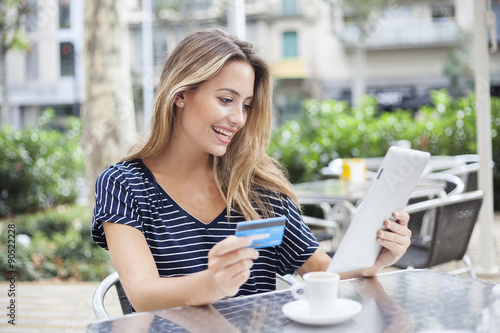 Woman buying online with a tablet and a credit card in a terrace bar