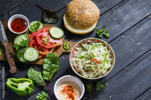 delicious veggie Burger. Raw ingredients - cabbage, tomato, cucumber, lettuce, pepper, sauce vegetarian and a homemade bun for burgers, on a dark wooden surface