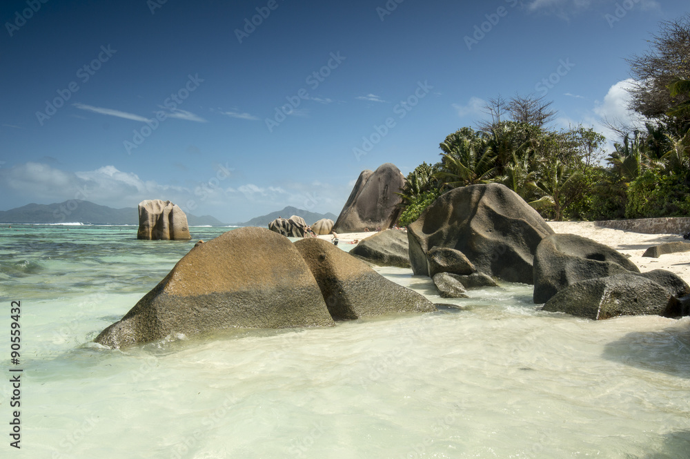 Naklejka premium View on untouched tropical beach Anse Source d'Argent with palm trees and bounders granite rocks, turquoise ocean and blue sky. Seychelles islands, La Digue.
