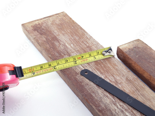 фотографія tape measure measuring width of plank with saw, construction tools and material