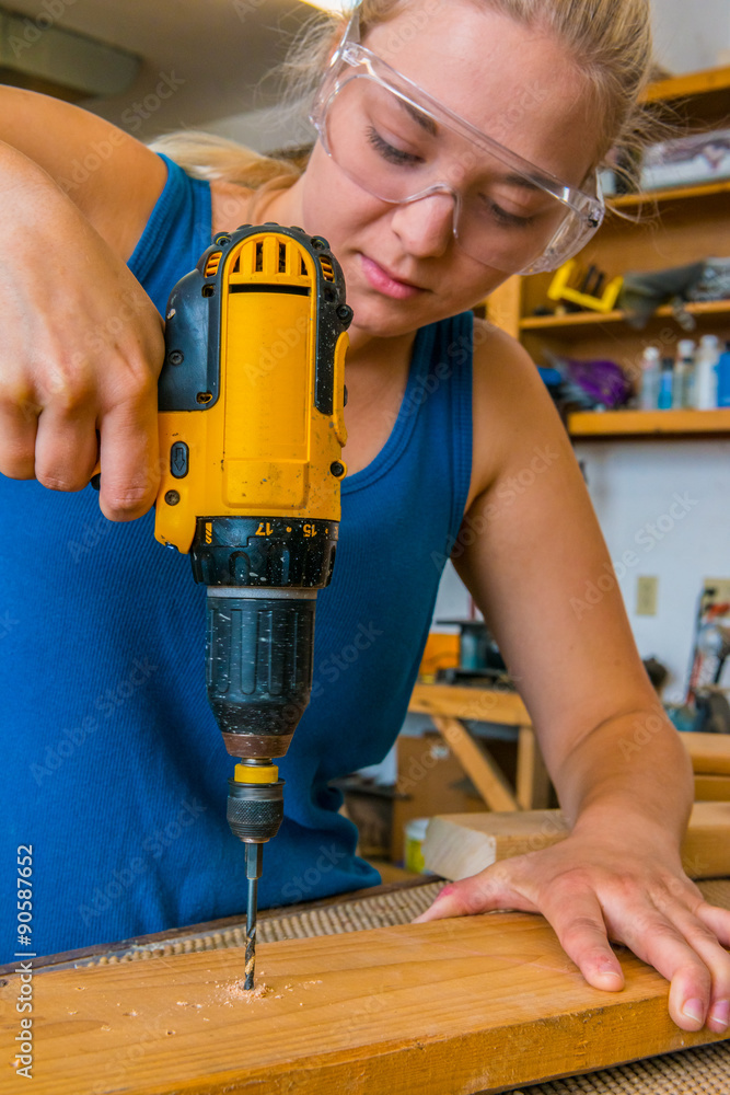 Caucasian young adult female woodworker using a power drill in workshop