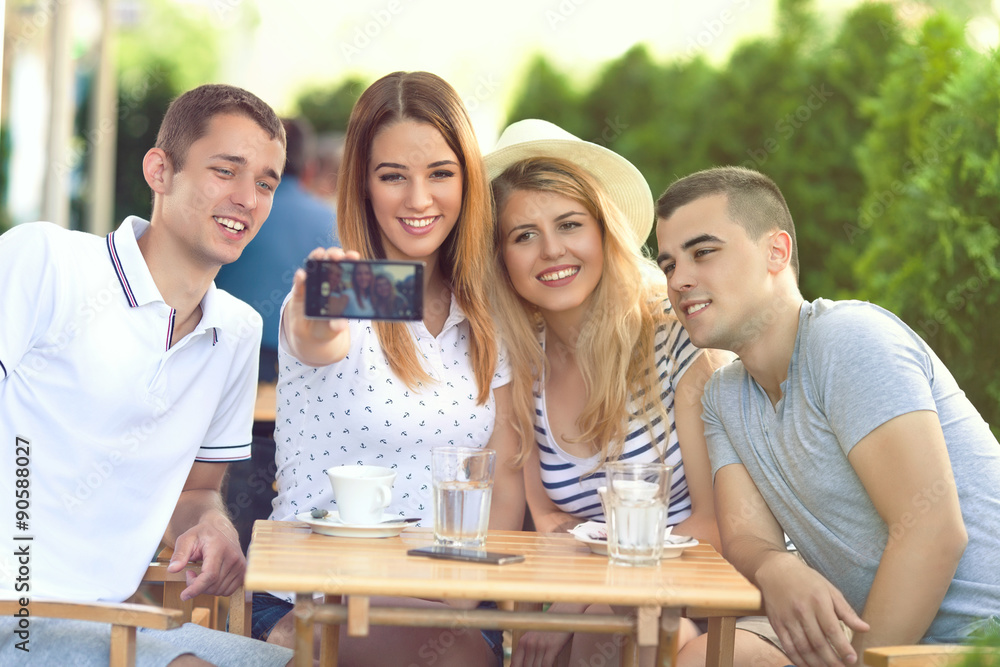 Fototapeta premium Group of teenage friends having fun in the outdoor cafe taking selfies