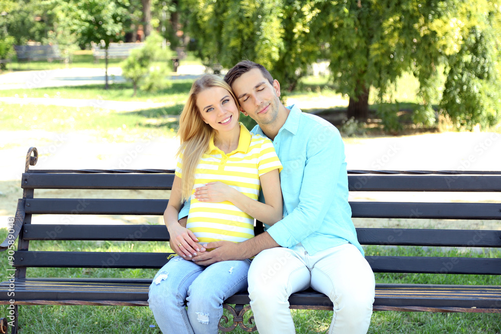 Young pregnant woman with husband sitting on bench in park Young pregnant woman with husband sitting on bench in park