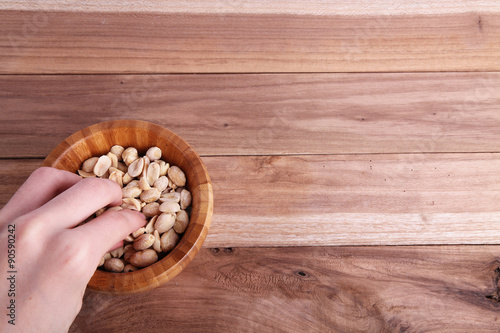 A hand picking some peanuts from a wooden bowl