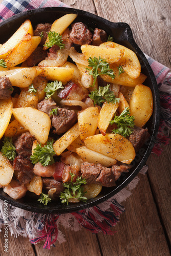 fried potatoes with meat and bacon in a pan close-up. vertical top view 