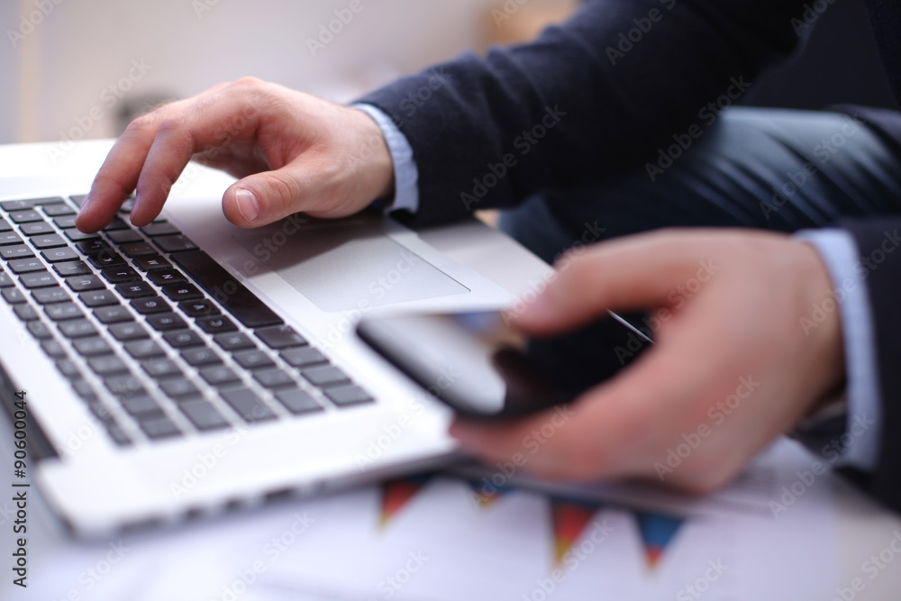Fototapeta premium Businessman at his workplace uses a smartphone and laptop