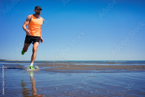 A man in a sports uniform is running along the shore of the lake © razoomanetu