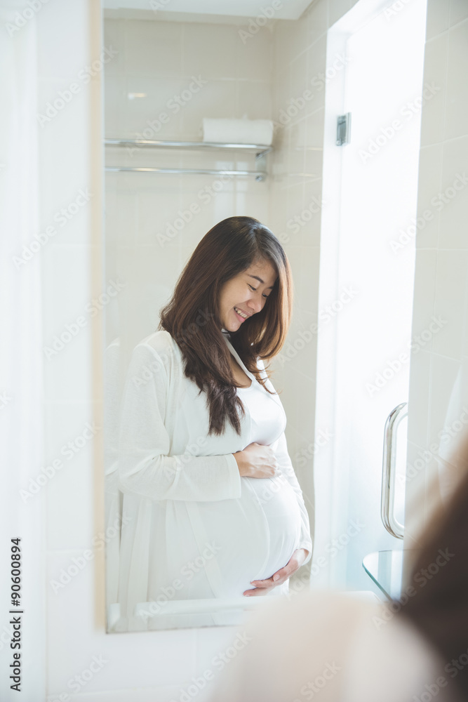 Asian pregnant woman posing in front of a mirror, smiling proudl Asian pregnant woman posing in front of a mirror, smiling proudl