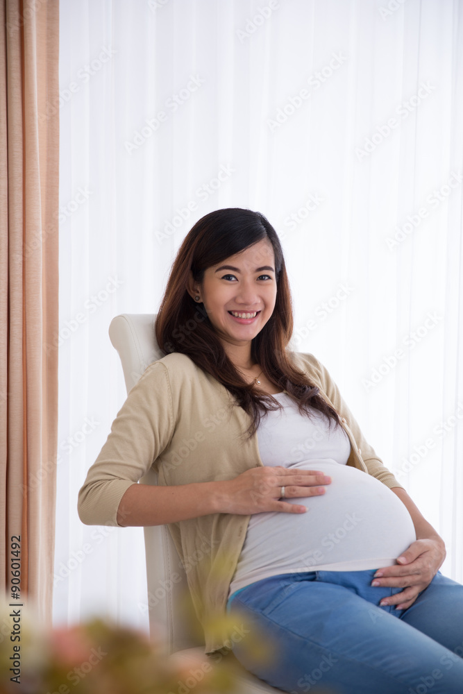 Happy pregnant asian woman touching her big belly while sitting