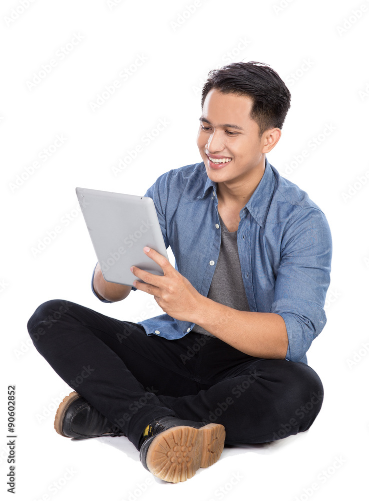 Young asian man using tablet pc while sitting on the floor, isol Young asian man using tablet pc while sitting on the floor, isol