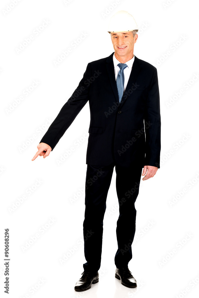 Smiling businessman with hard hat pointing down Smiling businessman with hard hat pointing down