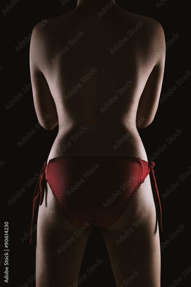 Naklejka premium Portrait of a topless Asian sexy woman in red lingerie showing her smooth skinned back isolated over black background.