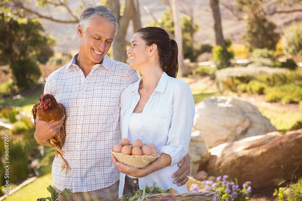 Smiling farmer couple holding chicken and eggs Smiling farmer couple holding chicken and eggs