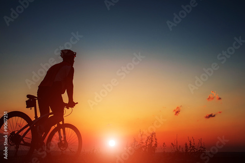 Silhouette of a biker and bicycle on sky background.