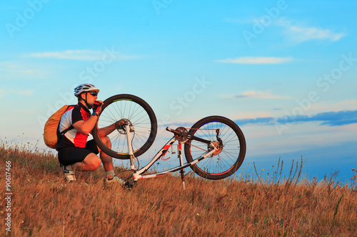 Man cyclist repairing a bike against blue sky
