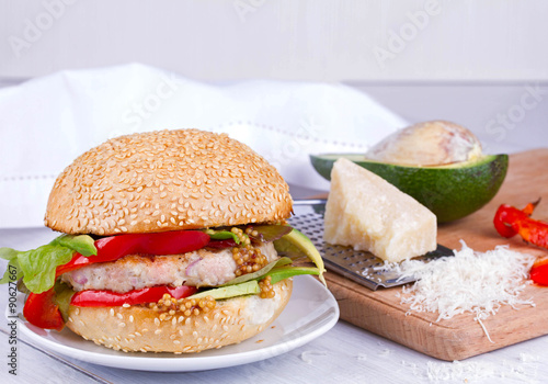 Home cooked burger with turkey, avocado, lettuce, onions, red paprika pepper on a sesame seed bun photo