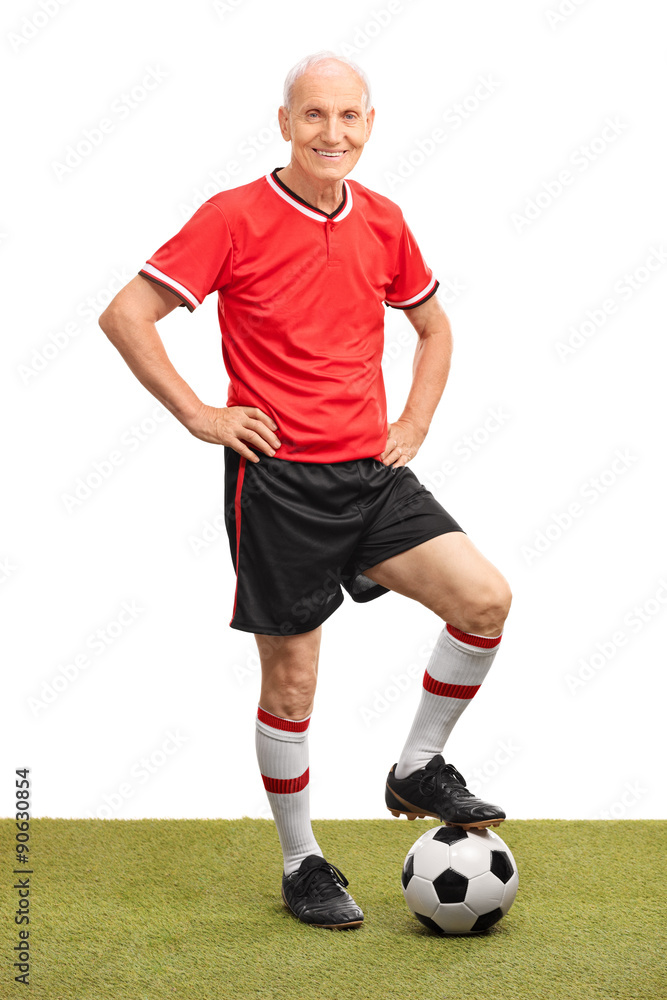 Senior man in a red jersey stepping over a football Senior man in a red jersey stepping over a football