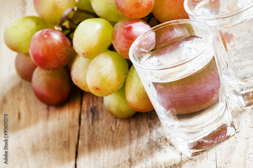 Grappa in a small glass and ripe grapes on old wooden table, sel