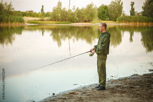 man in camouflage suit is fishing on the pond