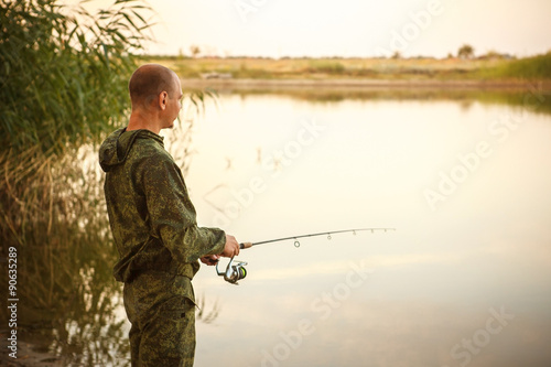 man in camouflage suit is fishing on the pond