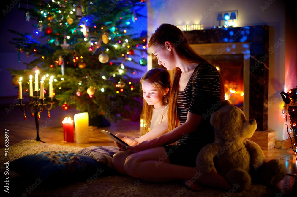 Mother and daughter using a tablet by a fireplace on Christmas Mother and daughter using a tablet by a fireplace on Christmas