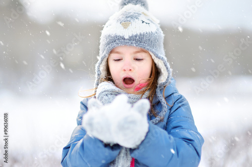 Funny little girl catching snowflakes in winter park