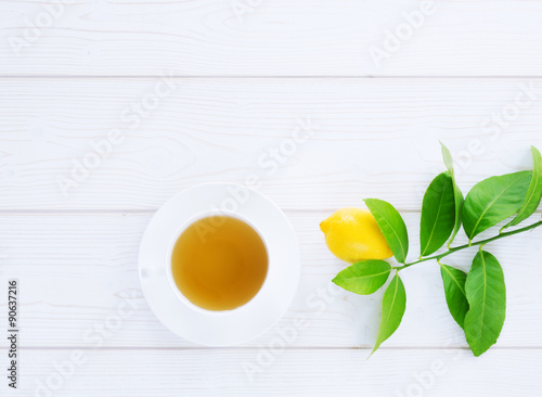 white cup with black tea and lemon yellow on a green branch on a white wooden background