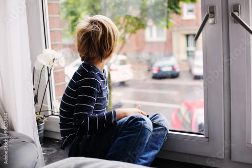 7 year old boy sitting near the window and looking to the street