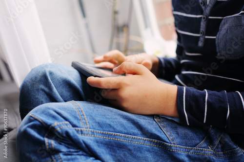 7 year old boy sitting near the window and playing tablet