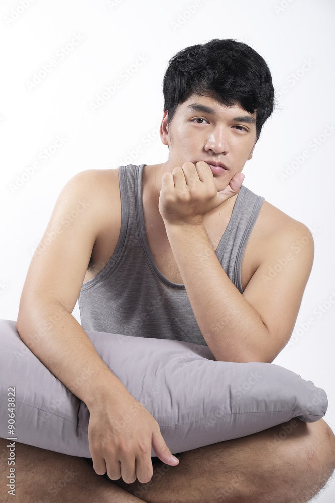 Asian man in grey pajamas sitting and holding the pillow Asian man in grey pajamas sitting and holding the pillow