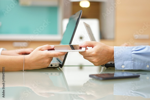 man is giving smart mobile phone to woman next to laptops, overu