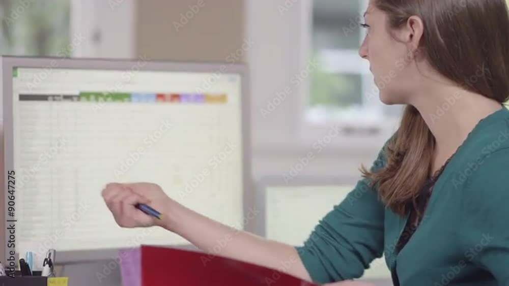 Close up of a business woman in a bright office jotting notes and entering data into a computer
Close up of a business woman in a bright office jotting notes and entering data into a computer