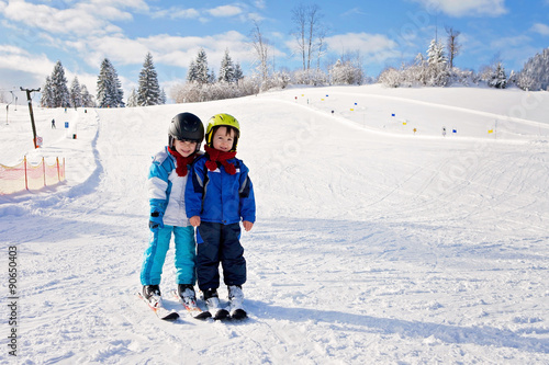 Two cute little boys, brothers, skiing on a sunny day