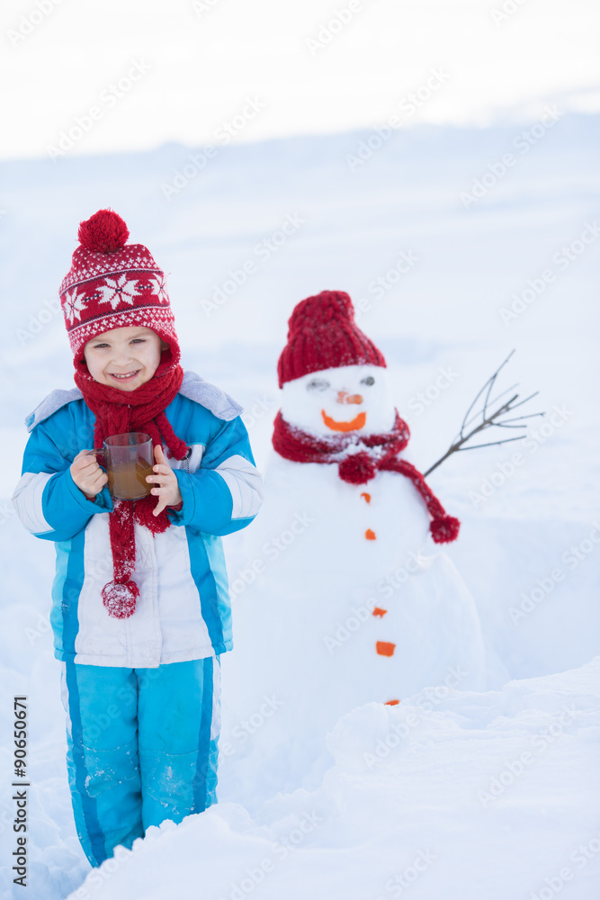 Happy beautiful child building snowman in garden, winter time, h Happy beautiful child building snowman in garden, winter time, h