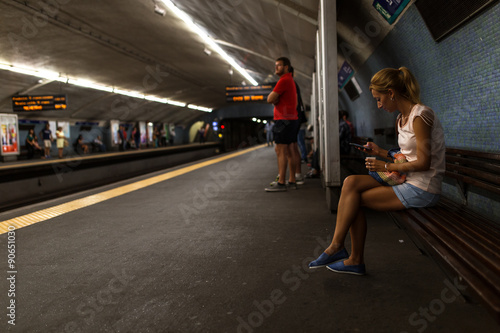 Female traveler standing at the metro station by night and using smart phone.
